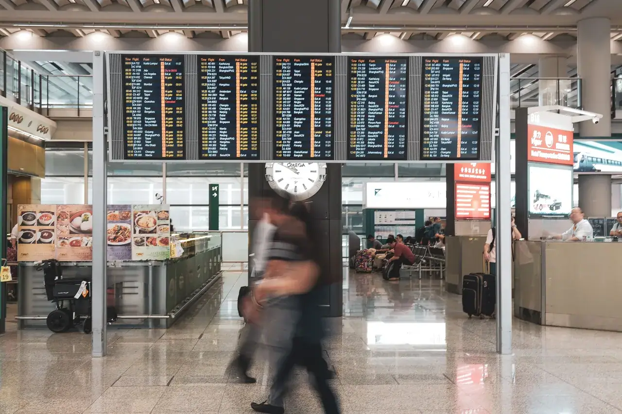 Utasok a repülőtéri terminálban, háttérben az indulási táblákkal
